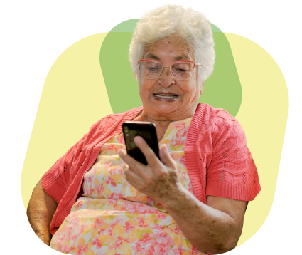 Mujer mayor con cabello blanco y gafas, vestida con un suéter rosa y un vestido floral, sonriendo mientras usa un smartphone, representando la seguridad ofrecida con cada recarga de saldo en Pronto Topup.